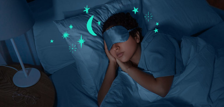 A woman wears a sleep mask with her head on a pillow in bed
