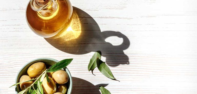 Image of a dish of ripe olives and oil on a table in the sunlight, evoking health and wellness