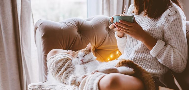 A cozy strong woman relaxes in a chair with a cat and warm beverage. Give back to your mom, sister, wife, or favorite strong women during the holidays.
