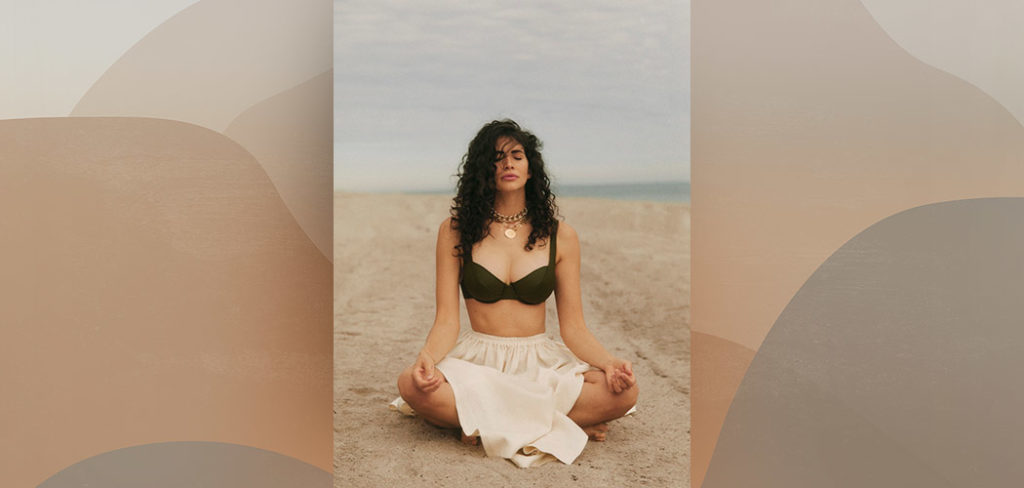 Hope Dworaczyk Smith meditating crossed-legged on the beach in her bathing suit