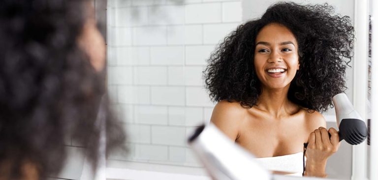 Woman blow-drying her hair while looking in the mirror after using a haircare product