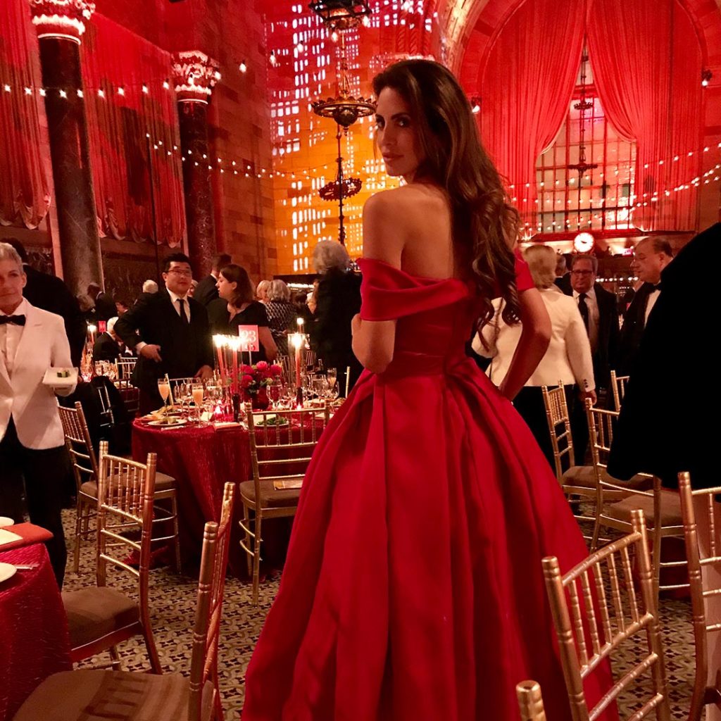 Hope Dworaczyk in a bright red gown stands at a dinner party