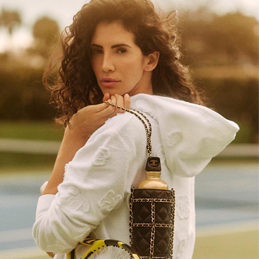 Hope Dworaczyk wears a jacket and poses with tennis racket on a tennis court