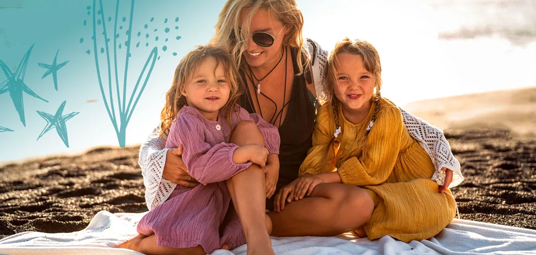 Mother and daughters cuddle together on a beach blanket enjoying a family vacation.