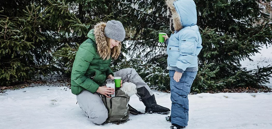 A mother and daughter in winter coats filling up cups from a tumbler.